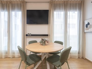 A dining area with a round table, four chairs, a flat-screen TV mounted on the wall, and sheer curtains. - Bright studio in a building with terrace (Málaga)
