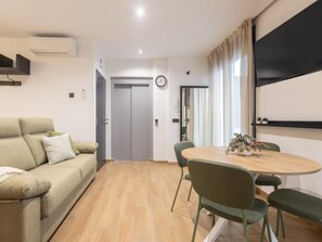A modern living room with a sofa, a dining table with chairs, a flat-screen TV mounted on the wall, and a door leading to another room. - Bright studio in a building with terrace (Málaga)