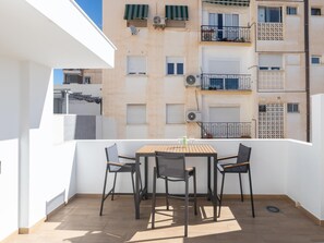 Un balcon doté d’une table en bois et de quatre chaises, offrant une vue sur un immeuble d’habitation avec des balcons et des unités de climatisation.