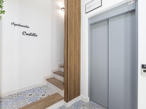Eine Treppe mit einer Holzvertäfelung an der Wand, einem Schild mit der Aufschrift 'Apartamentos Castillo' und einem Aufzug.