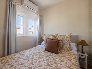 Una habitación de hotel con cama, mesita de noche, lámpara y aire acondicionado.