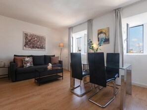 Ein modernes Wohnzimmer mit einer Couch, einem Couchtisch und zwei Sesseln. An der Wand hängt ein Gemälde und ein Fenster bietet einen Ausblick.