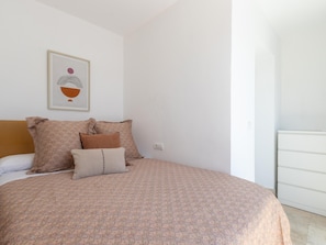 Cama bem arrumada com roupa de cama estampada, um travesseiro e um quadro na parede.