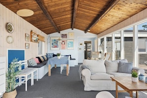 Ein gemütliches Interieur mit Holzbalkendecke, einem Essbereich mit Tisch und Stühlen, einer Couch und einem Fenster mit Blick auf eine Terrasse.