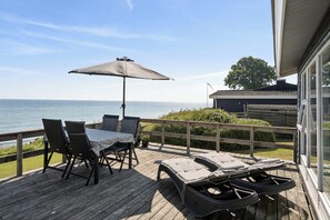 A wooden deck with a table and chairs, a large umbrella, and a view of the sea. - Seaside holiday home near beach and nature calm (Nyborg)