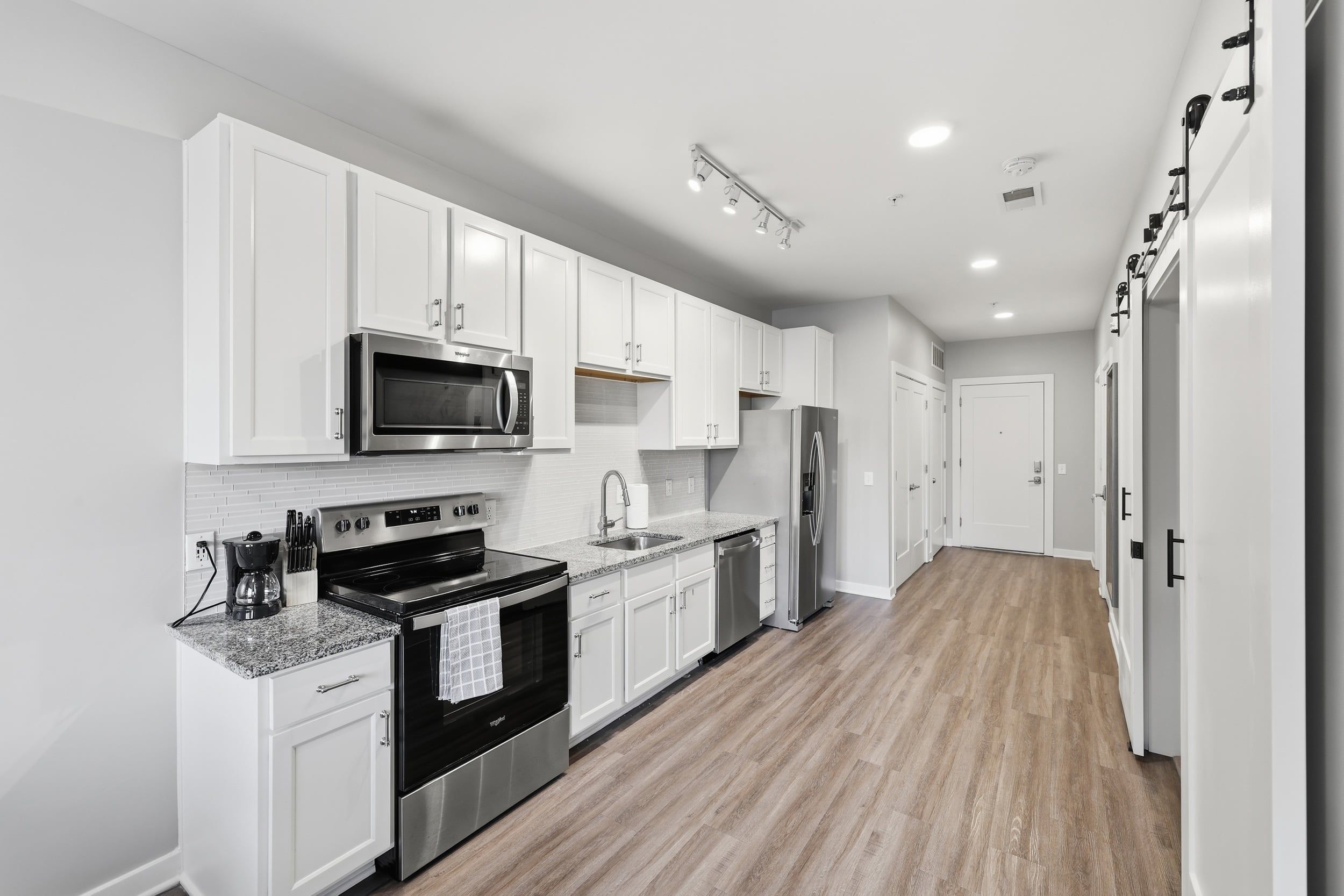 A modern kitchen with white cabinetry, stainless steel appliances, and a wooden floor.