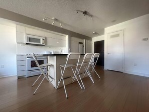 A modern kitchen with white cabinets, a microwave, and a stainless steel oven. There are three white chairs and a small table. - StayToronto - The CityPlace Escape (Toronto)