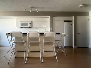 A modern kitchen with white cabinets, a microwave, and a refrigerator. There are three foldable chairs at the counter. - StayToronto - The CityPlace Escape (Toronto)