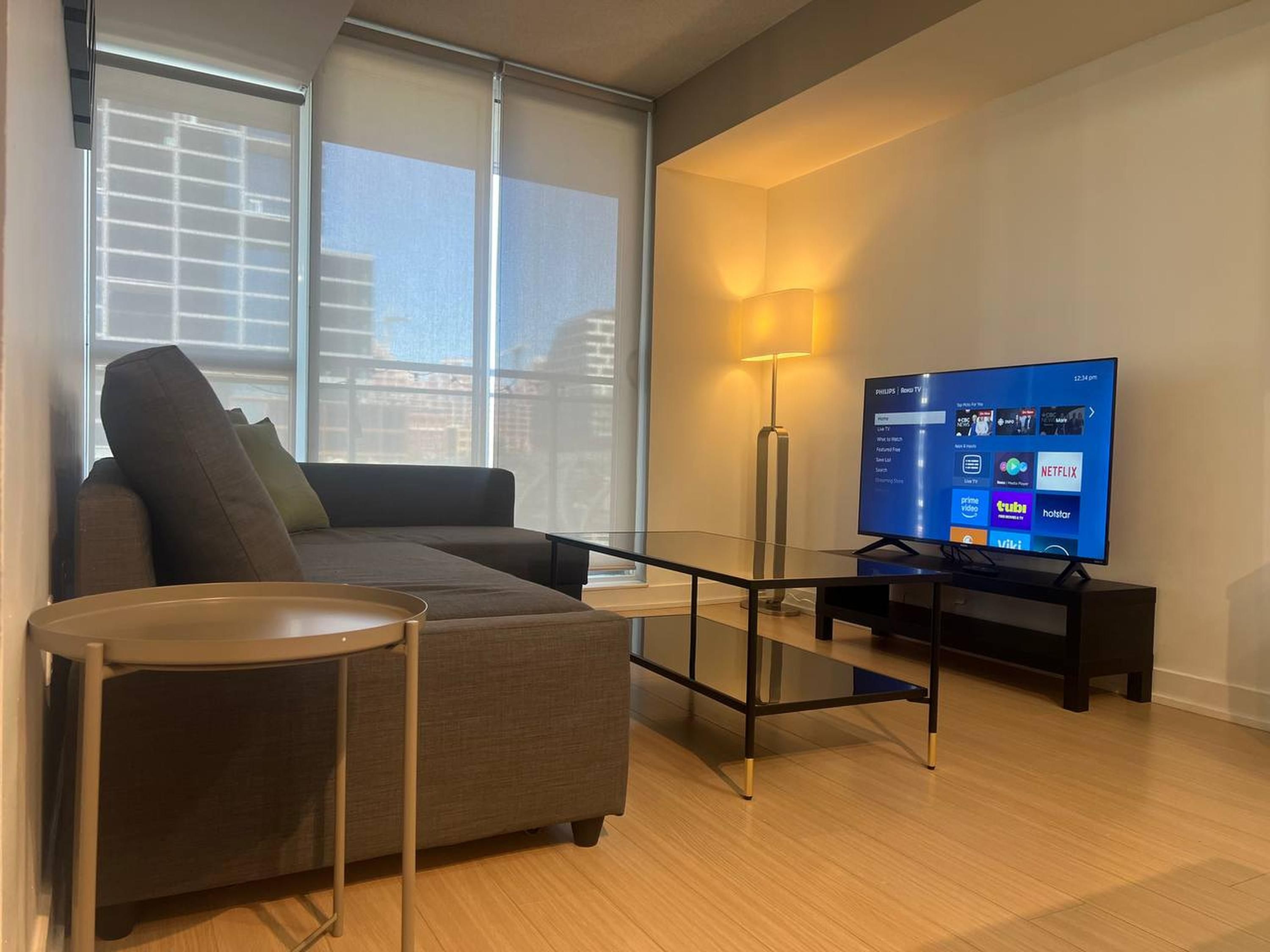A modern living room with a sofa, a glass coffee table, a TV on a stand, and a floor lamp.