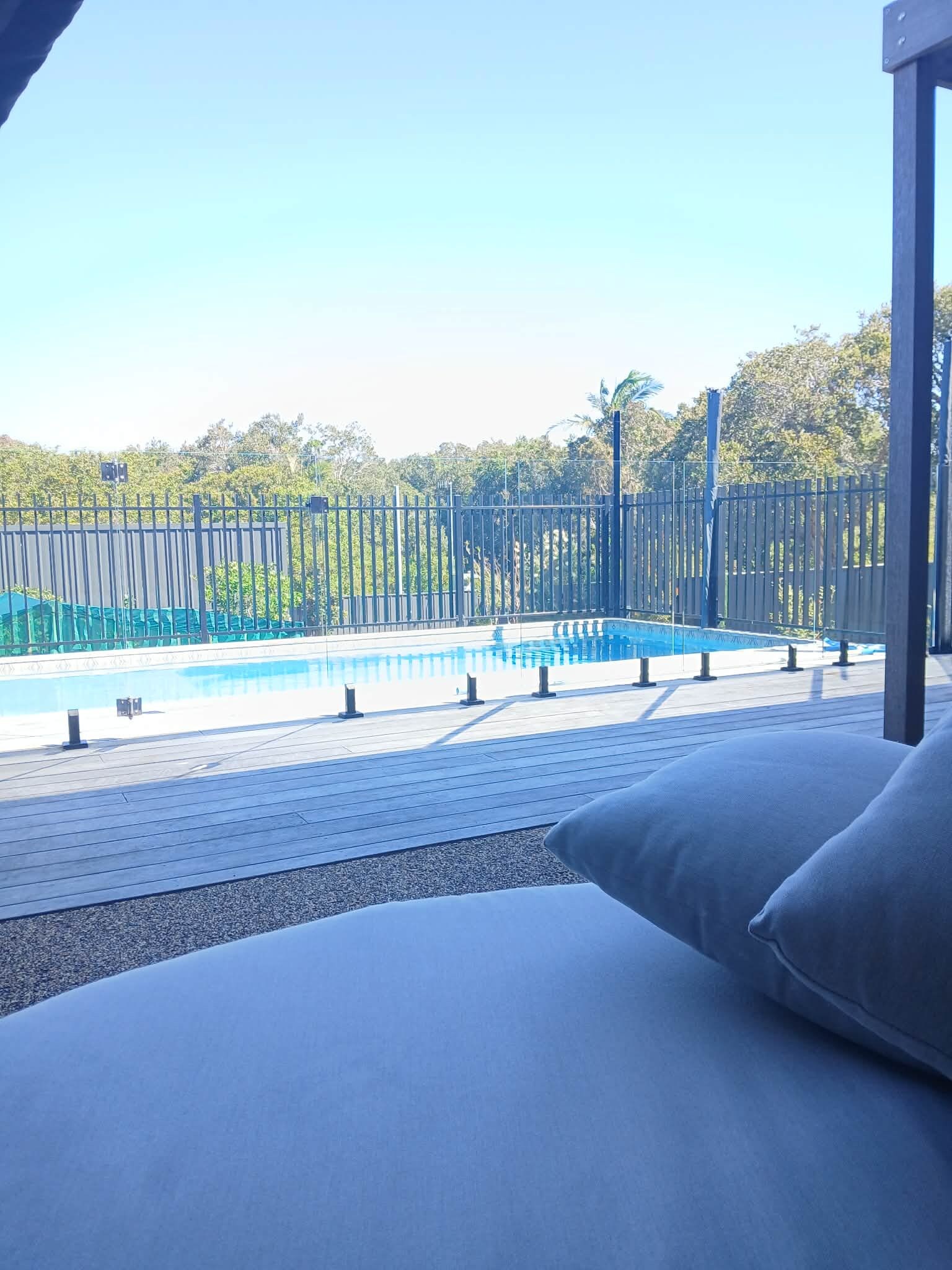 Un espace piscine offrant une vue sur un paysage boisé, une piscine clôturée et une partie d’un bâtiment dotée d’un balcon.