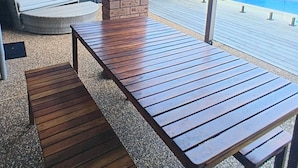 A patio area with a wooden table and bench, a brick pillar, and a view of a swimming pool. - Twin Beaches Arrawarra Headland (Arrawarra Headland)