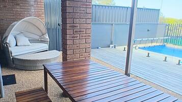 A patio area with a wooden table and bench, a brick pillar, and a view of a swimming pool.