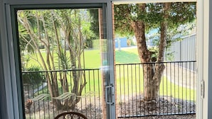 A room with a sliding glass door leading to an outdoor area with a metal fence, a tree, and a lawn. - Twin Beaches Arrawarra Headland (Arrawarra Headland)