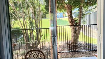 A room with a sliding glass door leading to an outdoor area with a metal fence, a tree, and a lawn.