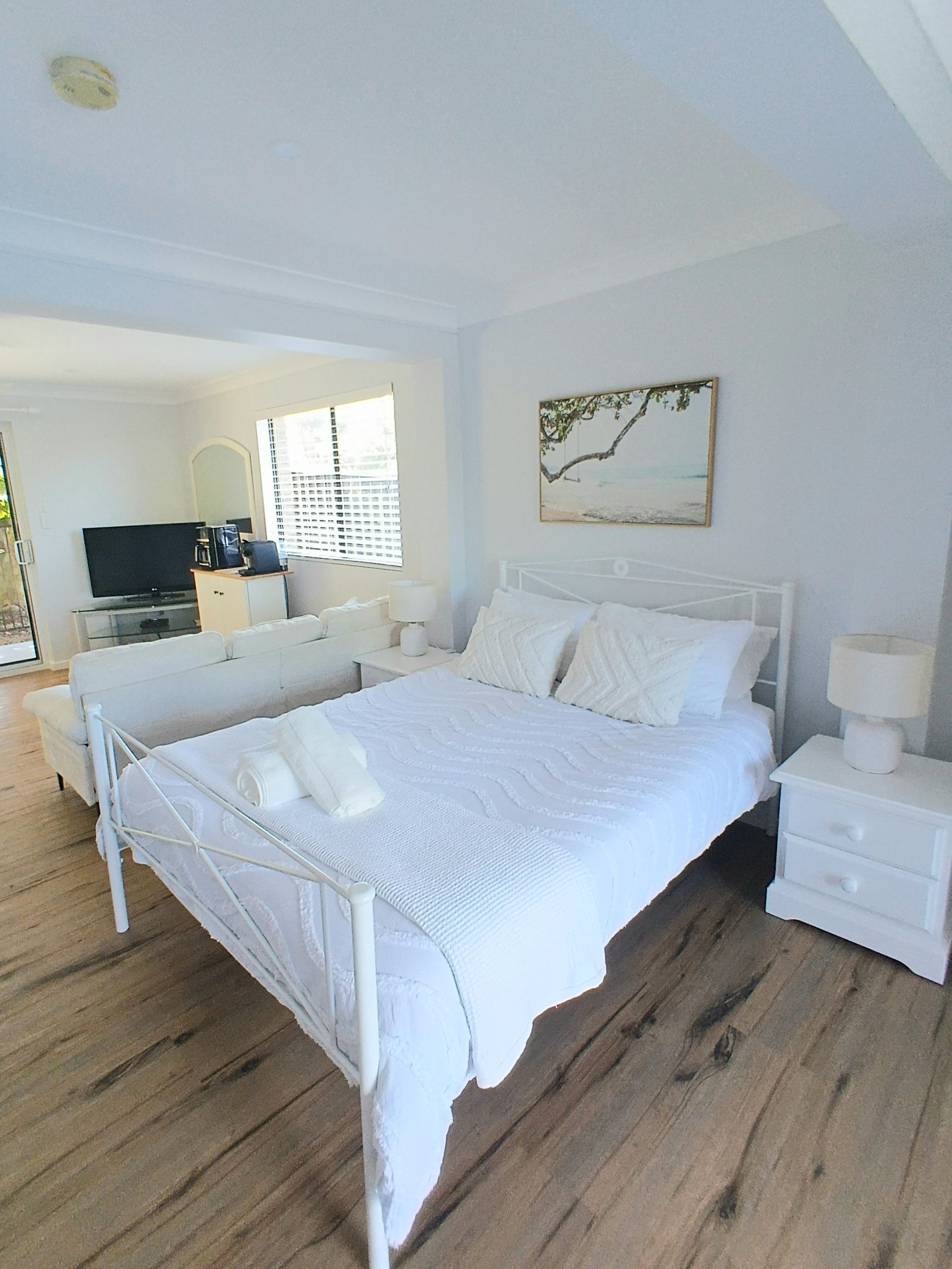 A bedroom with a bed, bedside tables, a television, and a window with blinds.