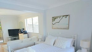 A bedroom with a bed, bedside tables, a television, and a window with blinds. - Twin Beaches Arrawarra Headland (Arrawarra Headland)