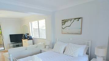 A bedroom with a bed, bedside tables, a television, and a window with blinds.