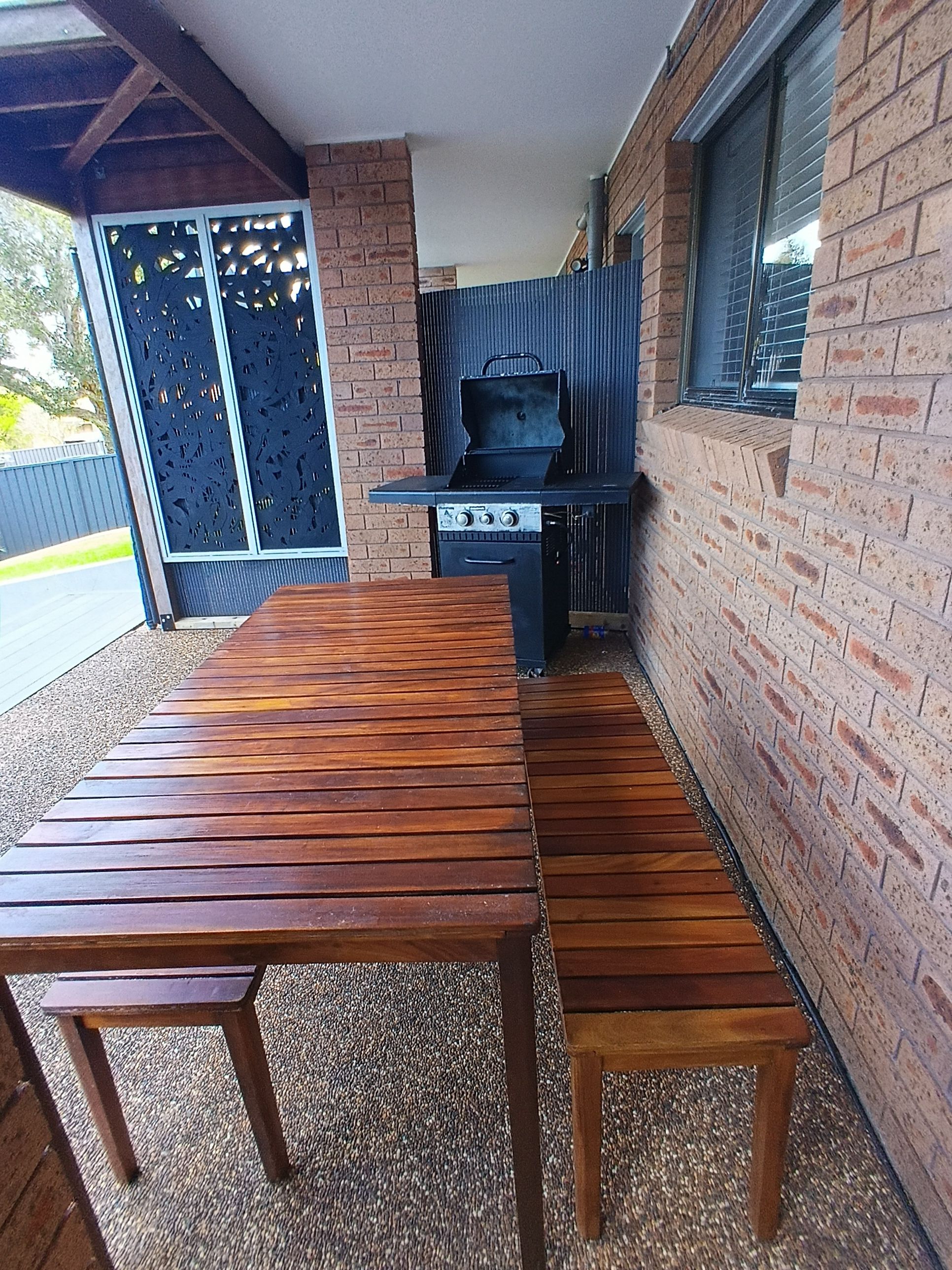 An outdoor patio with a wooden table and a barbecue grill.