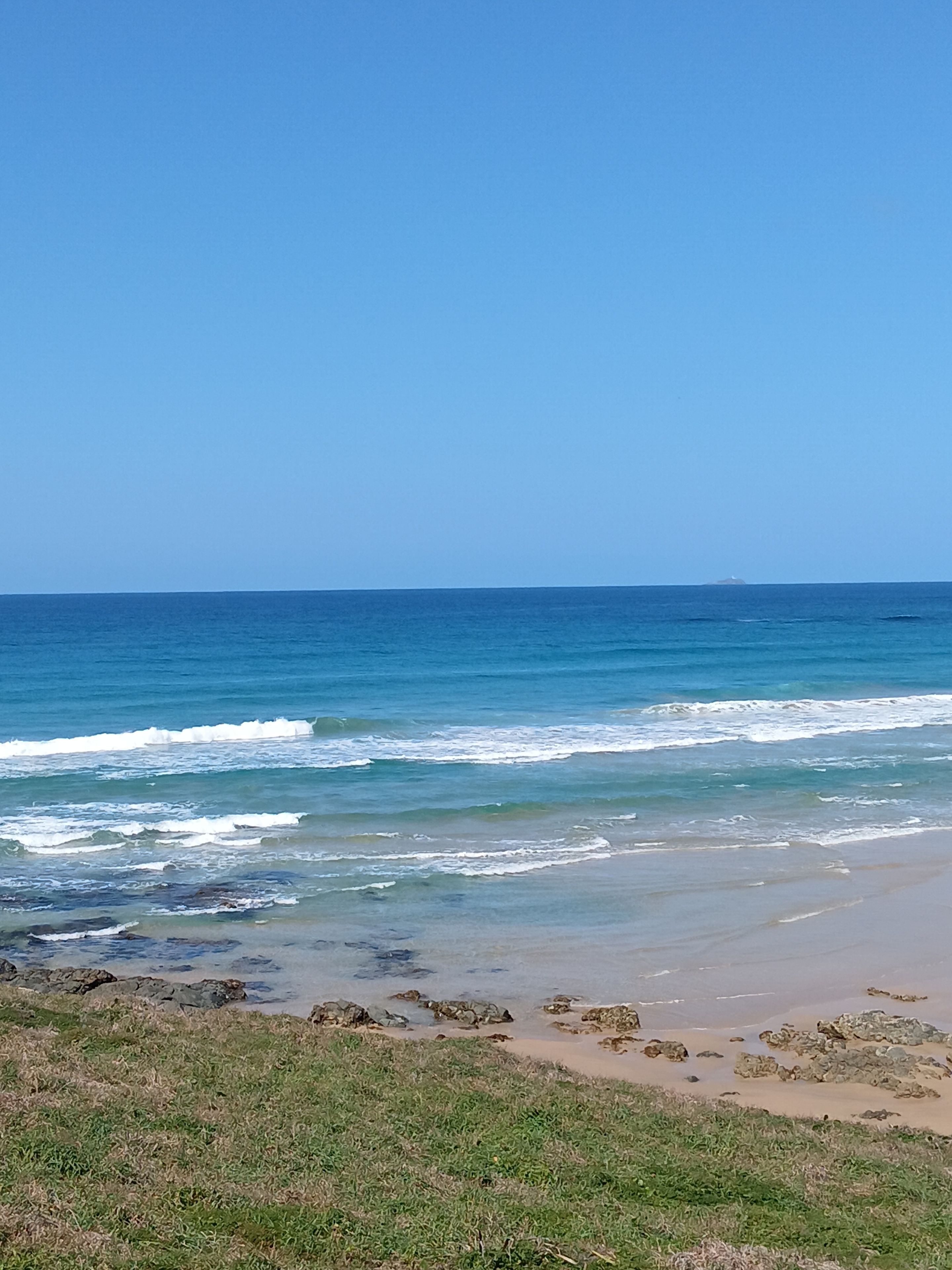 A beach with waves, a clear sky, and distant land.