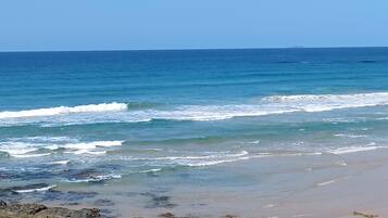 A beach with waves, a clear sky, and distant land.
