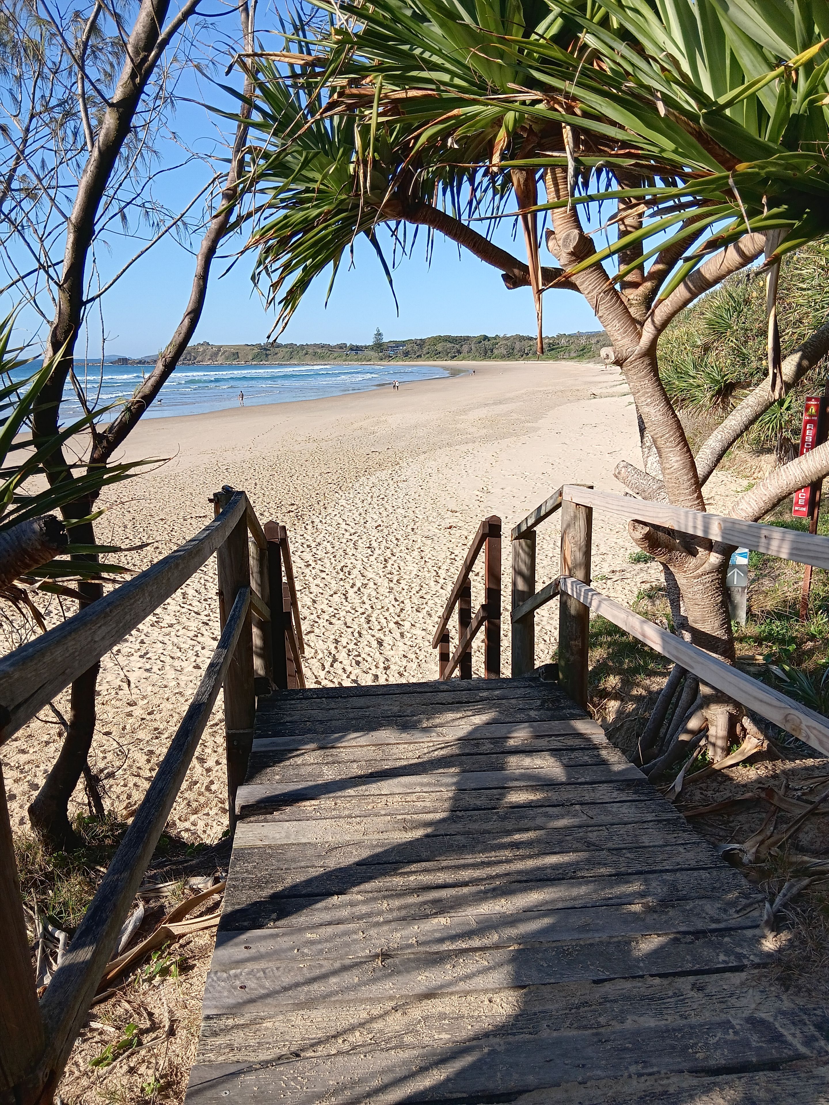 Un sentier en bois mène à une plage de sable fin, d’où l’on a une vue dégagée sur l’océan.