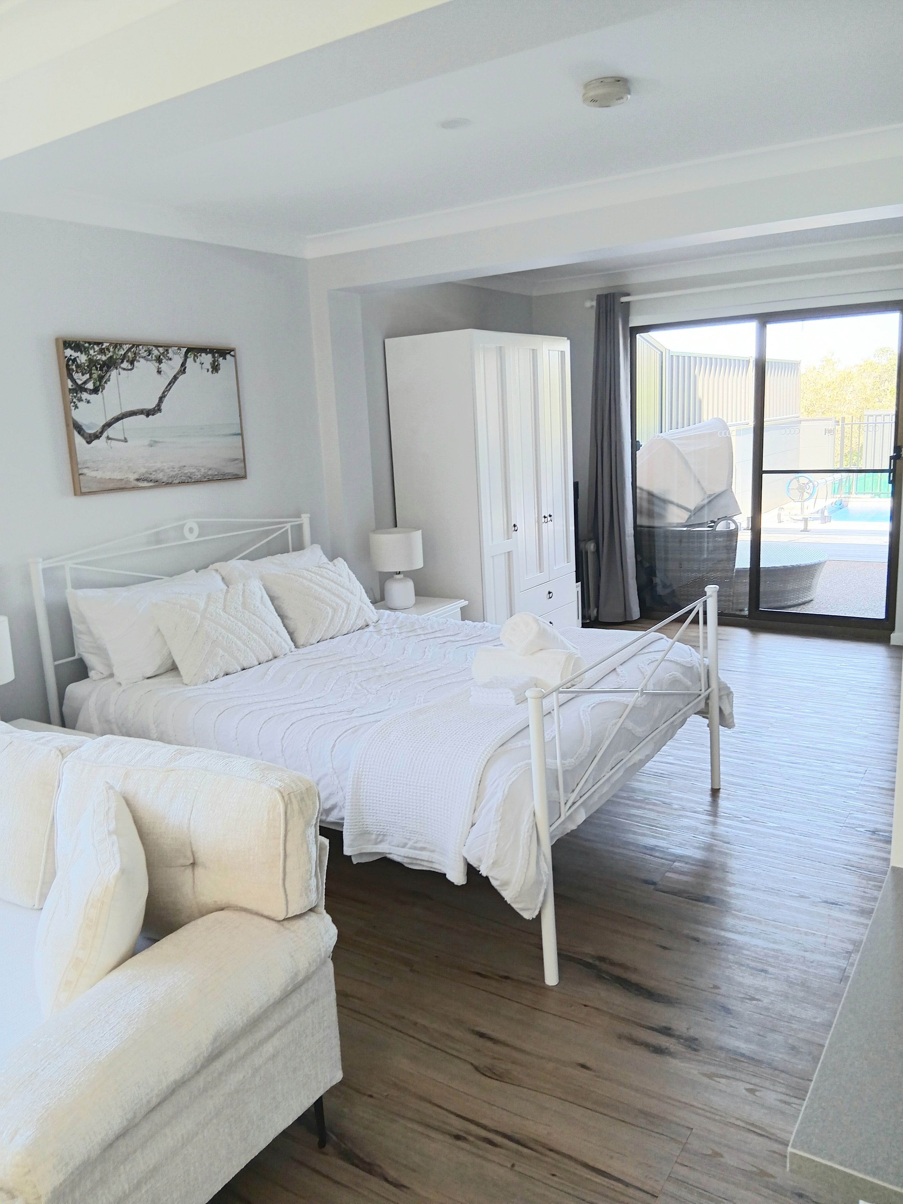 Un dormitorio con cama, una silla, un armario y vistas al exterior.