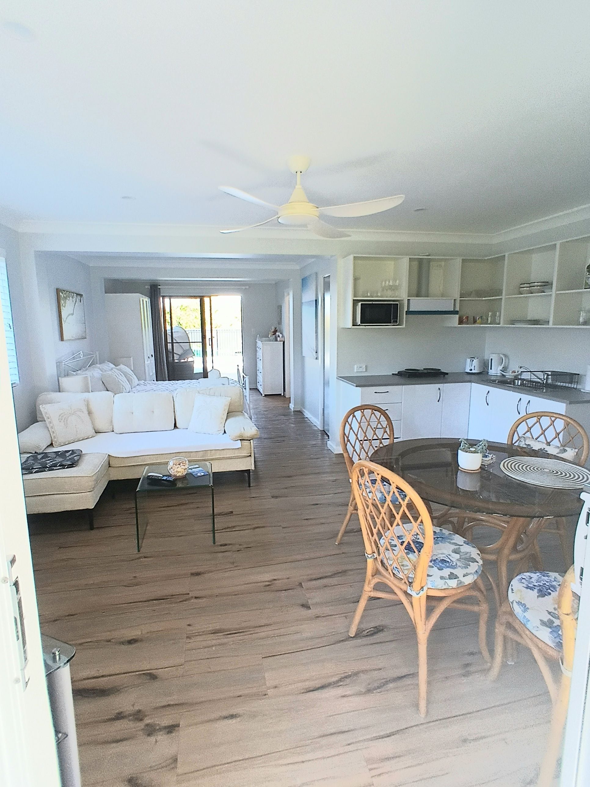 A spacious living area with a sofa, dining table, and chairs, a kitchen with cabinets, and a ceiling fan.