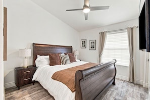 A bedroom with a bed, nightstand, lamp, ceiling fan, window with curtains, and framed pictures on the wall. - 4-bedroom Retreat in Scottsdale with Heated Pool, Firepit, Putting Green/Games (Scottsdale)