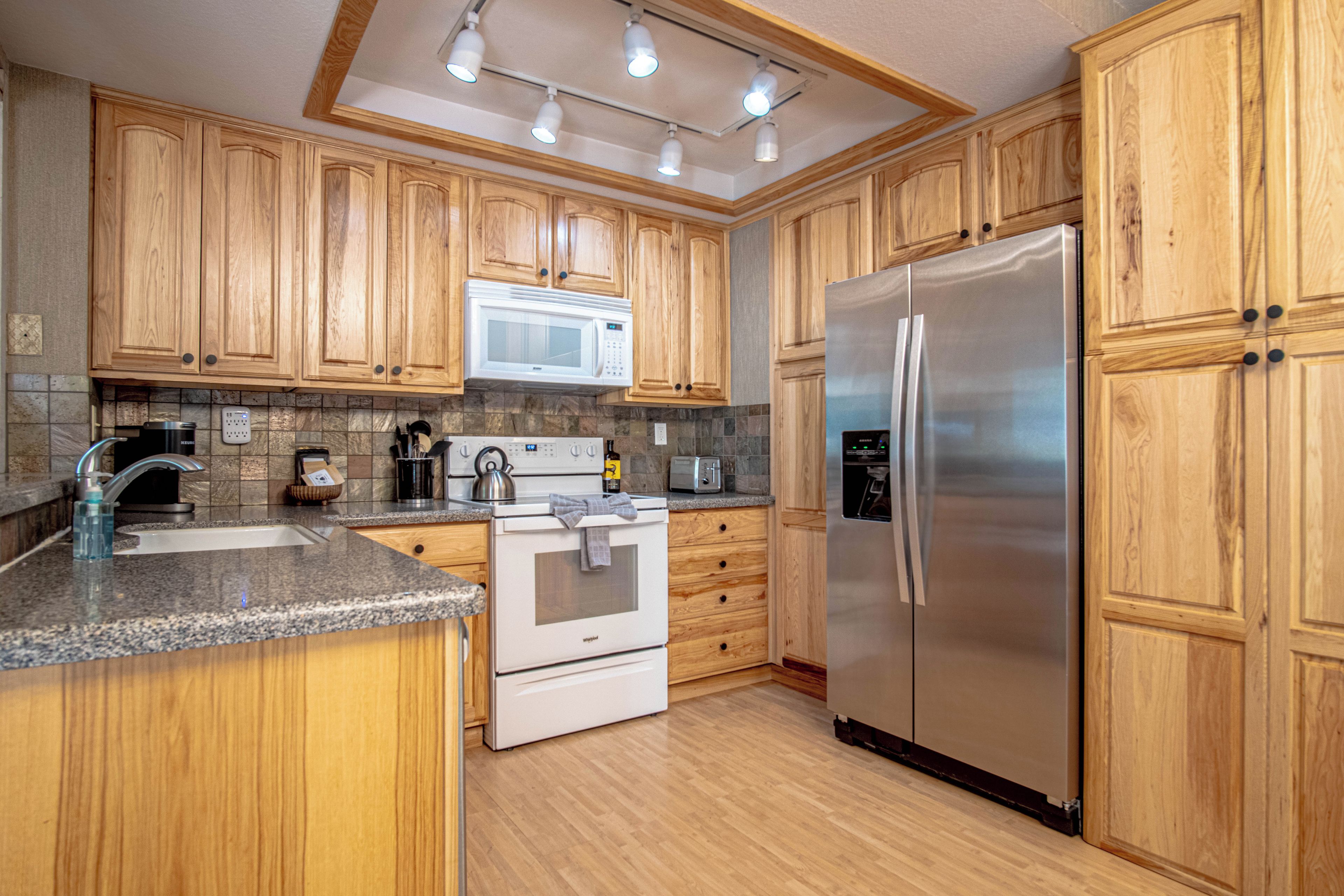 A kitchen with wooden cabinets, a stainless steel refrigerator, a microwave, a stove, and a sink.