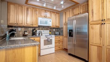 A kitchen with wooden cabinets, a stainless steel refrigerator, a microwave, a stove, and a sink.