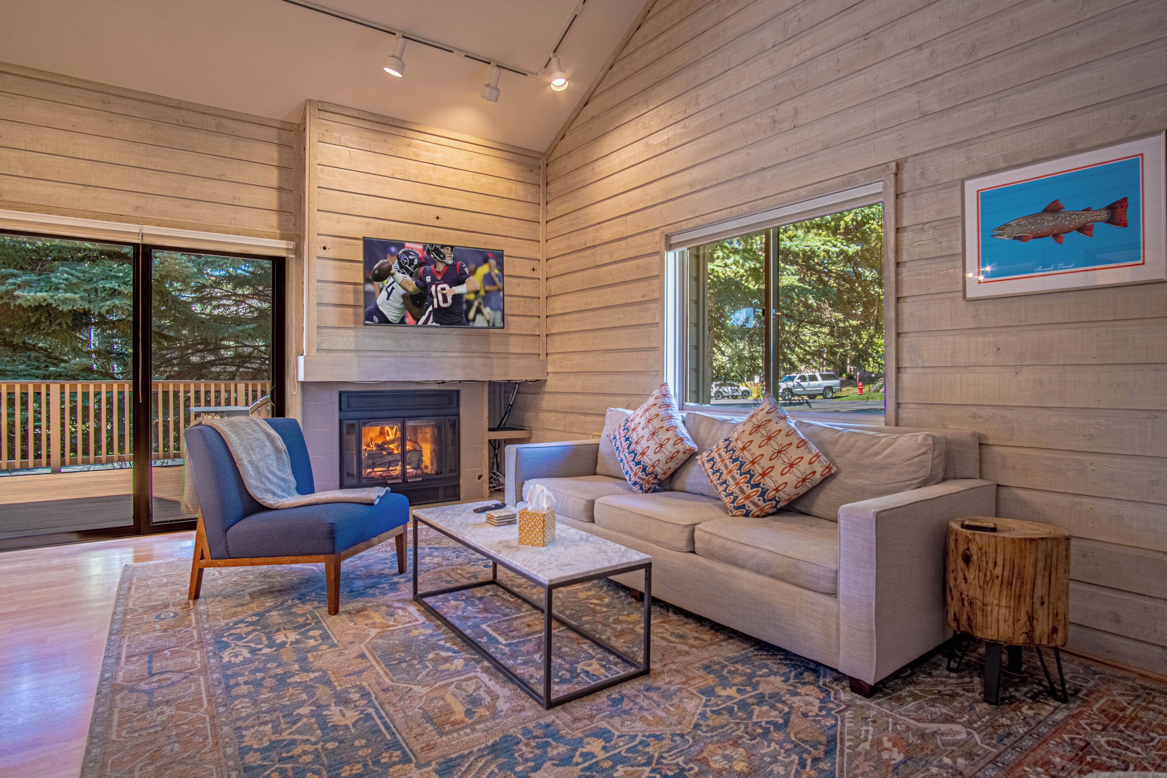 A cozy living room with a fireplace, comfortable seating, and a large window offering a view of the outdoors.