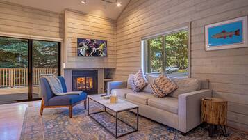 A cozy living room with a fireplace, comfortable seating, and a large window offering a view of the outdoors.