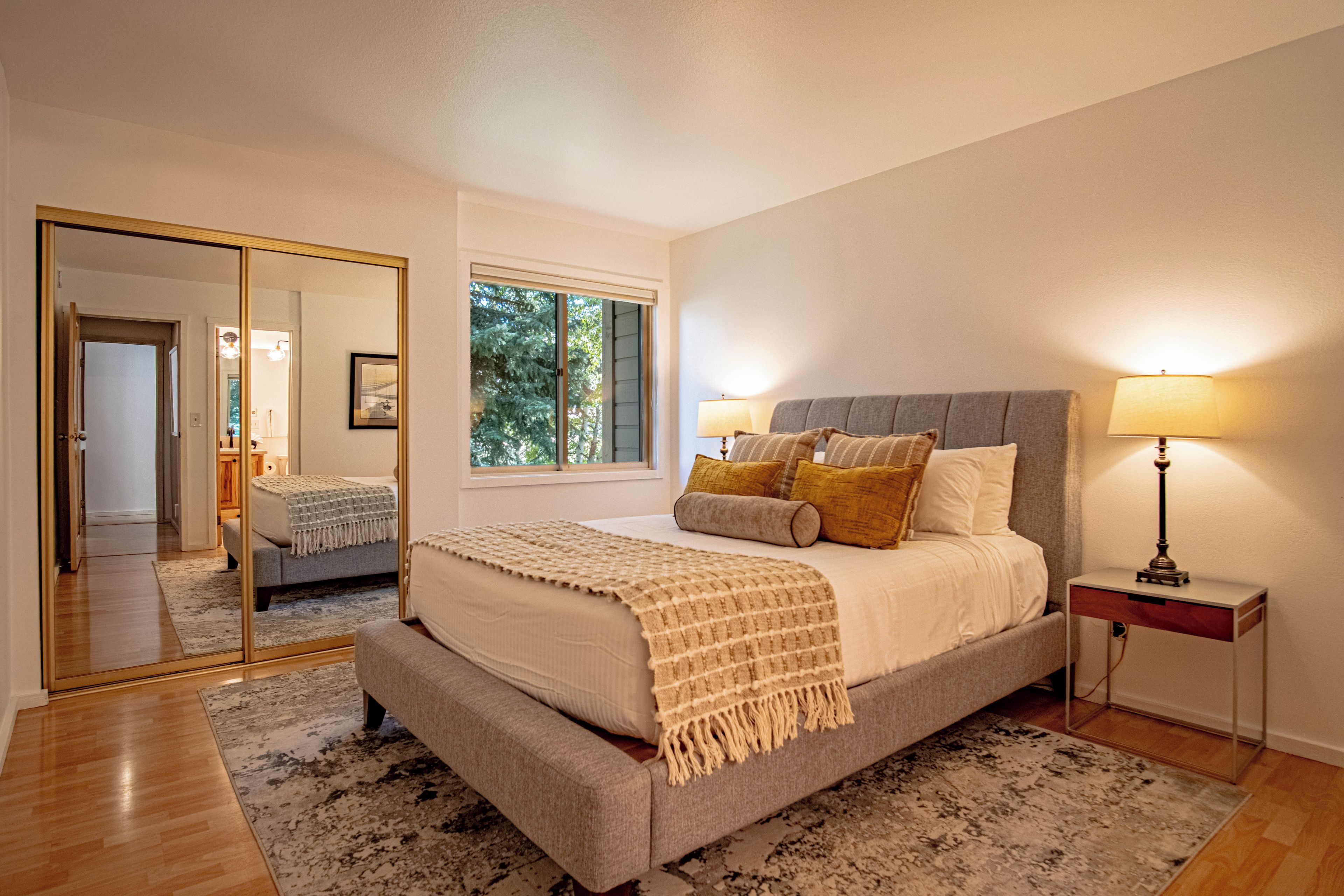 A bedroom with a large bed, bedside lamps, a mirror, and a window.