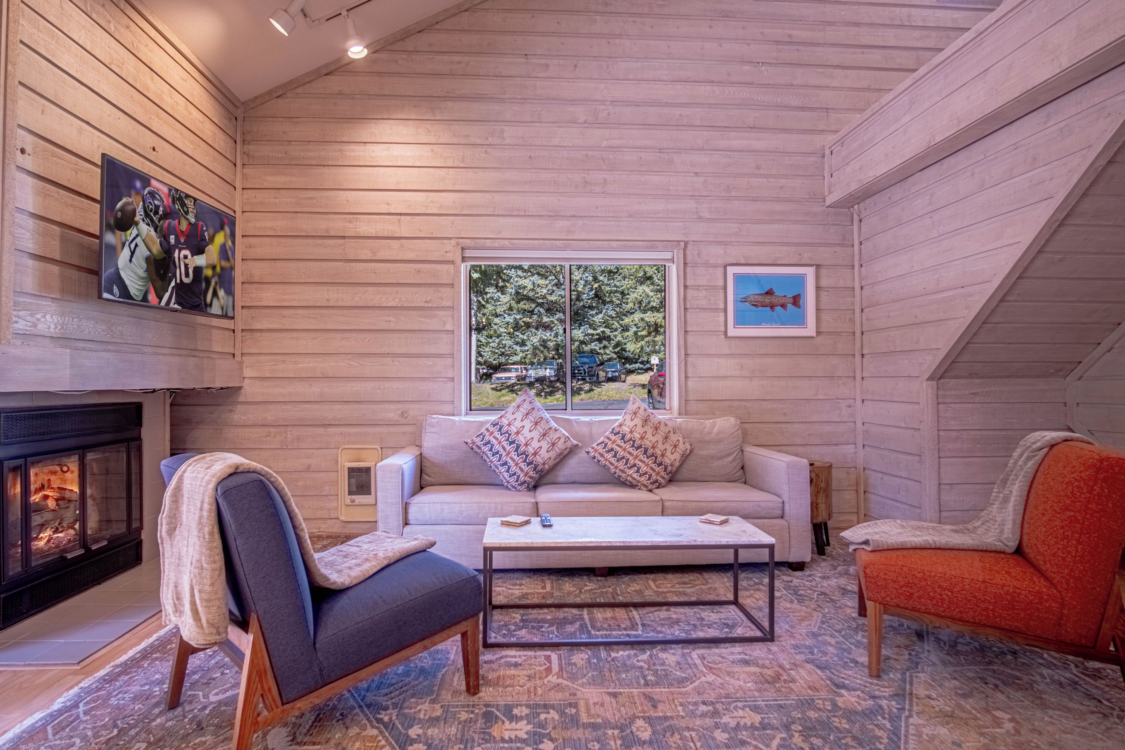 A cozy interior with a fireplace, a sofa, a coffee table, and a window with a view of trees.