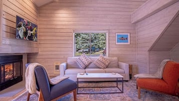A cozy interior with a fireplace, a sofa, a coffee table, and a window with a view of trees.