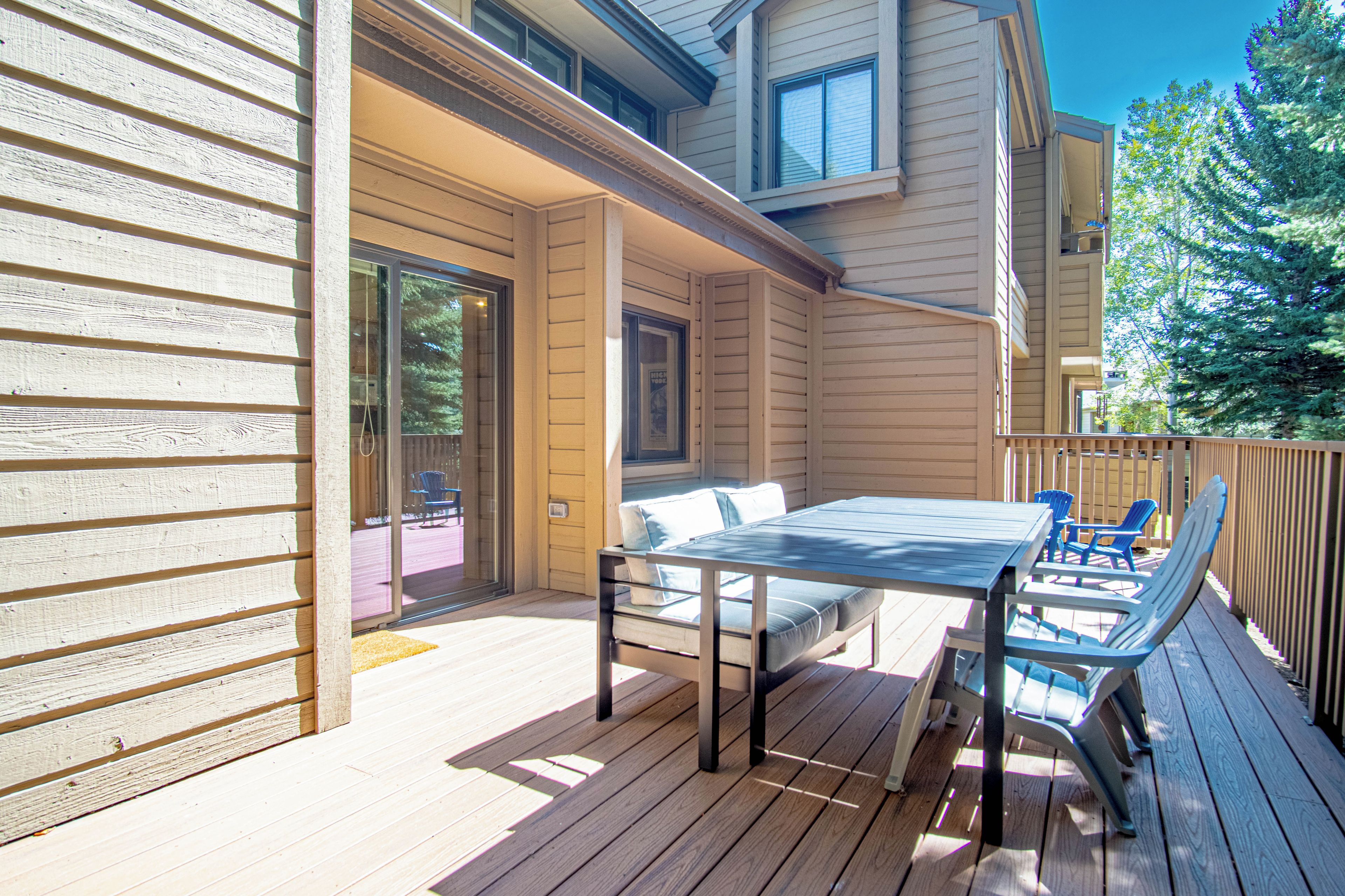 A wooden deck with a table and chairs, a sliding glass door, and a view of a tree.