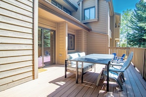 A wooden deck with a table and chairs, a sliding glass door, and a view of a tree. - 3BR Elkhorn Village condo with pool, hot tub, fireplace, and mountain access. (Sun Valley)