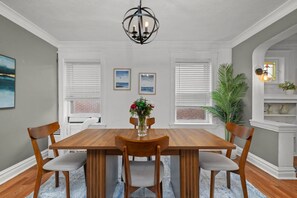Une salle à manger avec une table en bois, six chaises, un lustre et des œuvres d’art encadrées accrochées aux murs.