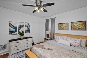 Ein Schlafzimmer mit einem Bett, einem Nachttisch, einer Kommode, einem Deckenventilator und Wandbildern.