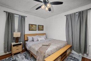 Une chambre à coucher comprenant un lit, une table de chevet, une lampe, un ventilateur de plafond et deux tableaux accrochés au mur.