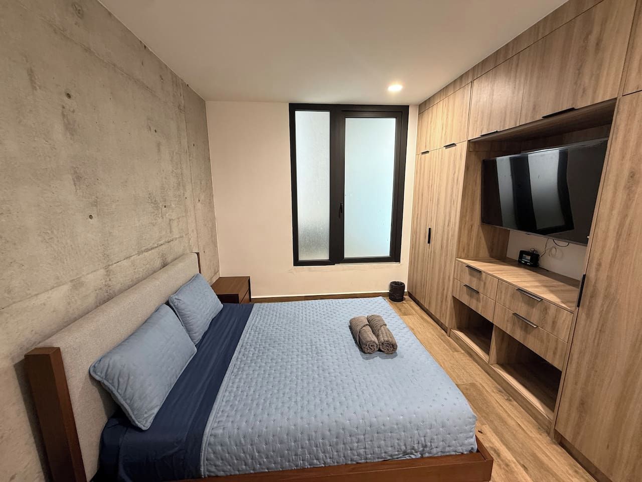 Un dormitorio con cama, ventana, televisión y muebles de madera.