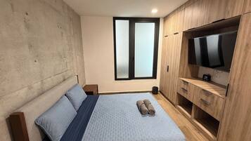 Un dormitorio con cama, ventana, televisión y muebles de madera.