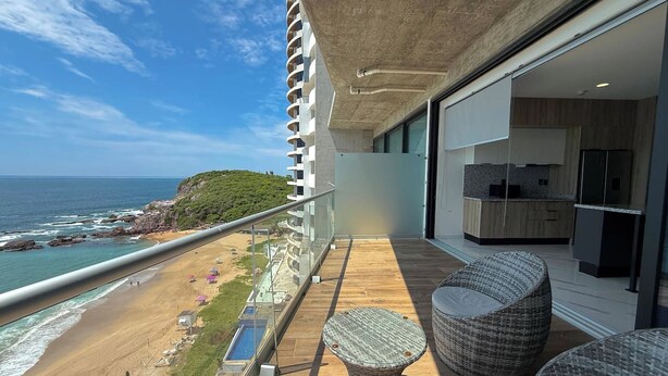 Ein Balkon mit Blick auf Strand und Meer, mit Korbmöbeln und einer modernen Küchenzeile.