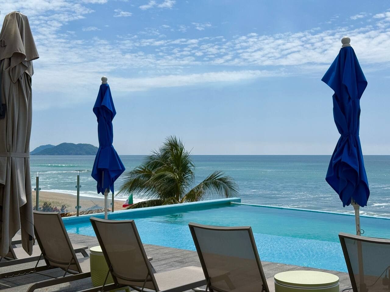 Un espace aménagé au bord de la piscine, avec des chaises longues et des parasols, offrant une vue sur la plage et l’océan.