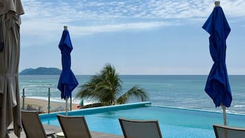 Un espace aménagé au bord de la piscine, avec des chaises longues et des parasols, offrant une vue sur la plage et l’océan.