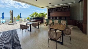Ein moderner Essbereich im Freien mit Meerblick, ausgestattet mit Holztischen und Korbstühlen, einer Bar mit Theke sowie einer Decke mit Einbaustrahlern.