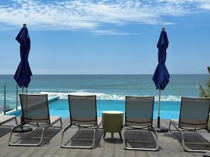 Un espace aménagé au bord de la piscine, avec des chaises longues et des parasols, offrant une vue sur l’océan.