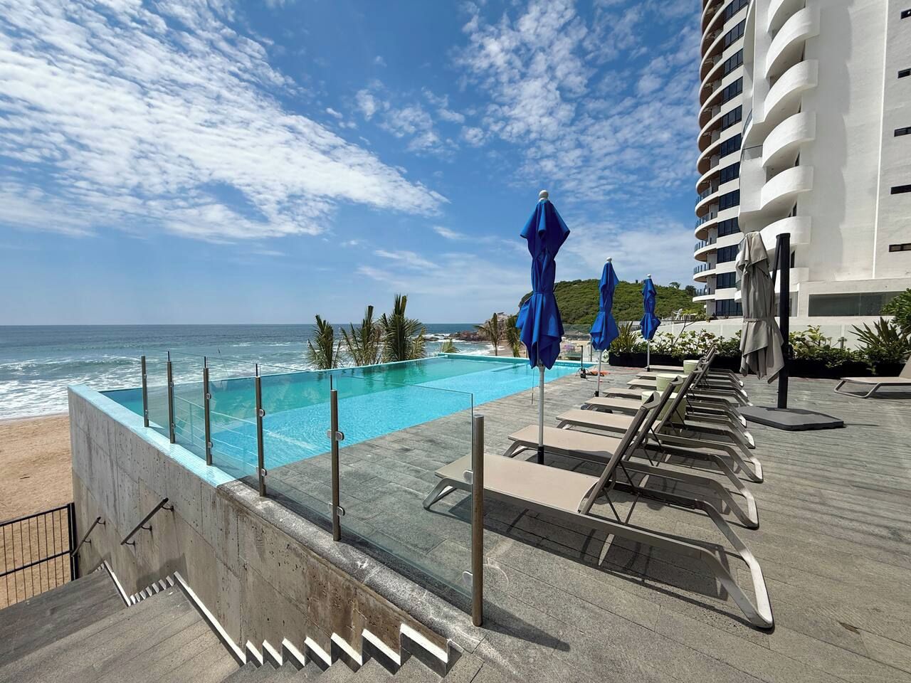 A rooftop pool with a view of the ocean, lounge chairs, and umbrellas.