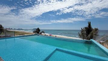 Un cielo azul despejado con nubes, una piscina y una playa al fondo.