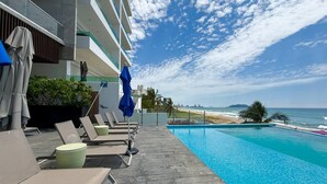 Ein Poolbereich mit Liegestühlen und Sonnenschirmen mit Blick auf einen Strand und das Meer.